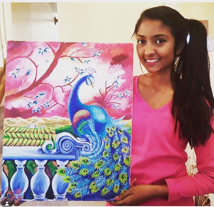 Artist holding a peacock painting in blossom pinks